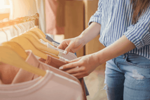 A woman in a striped blue shirt searching a rack of wooden hangers holding lightweight sweaters 