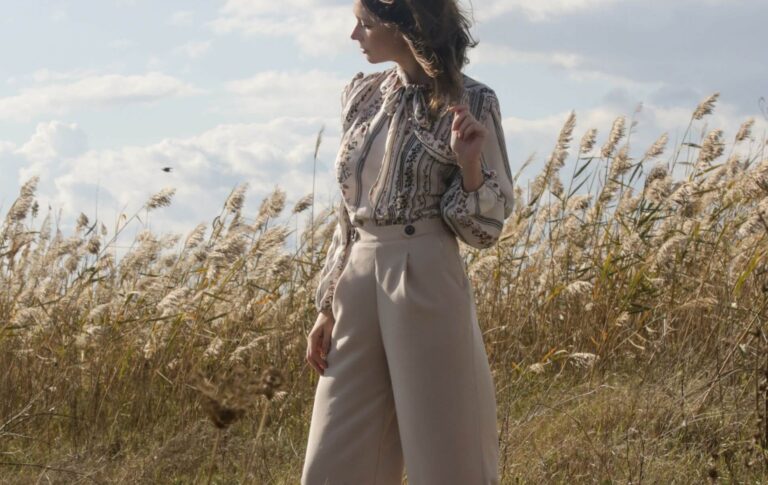 A petite woman standing in a field with beige wide legged pants and a striped blouse