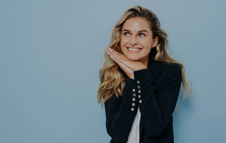 an image of an elegant woman who is wearing a dark jacket and her hands together on her chin who is very happy because someone has said she's elegant as a compliment