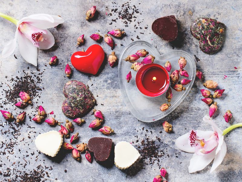 What is the Deeper Meaning of Valentine’s Day? - this is an image of hearts, candles, and rose petals scattered on a table top