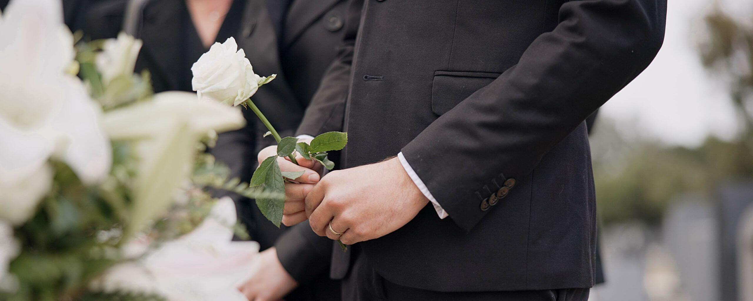 Funeral - a man holding a flower in front of a casket