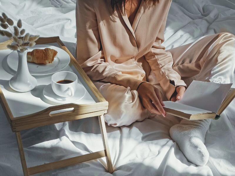 Elegant woman sitting on bed while reading and drinking a coffee