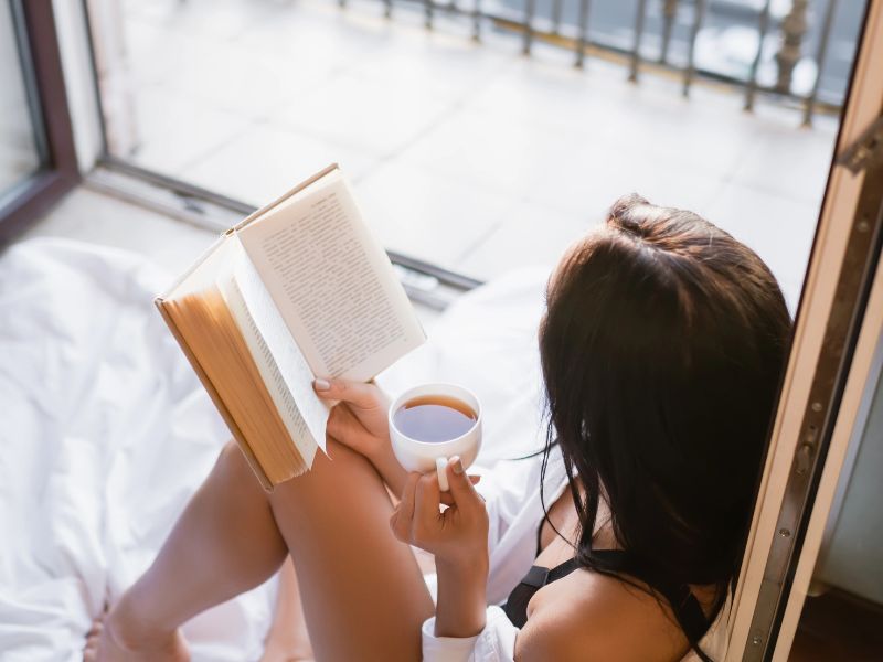 10 Minute Elegant Habits and a woman reading on a balcone